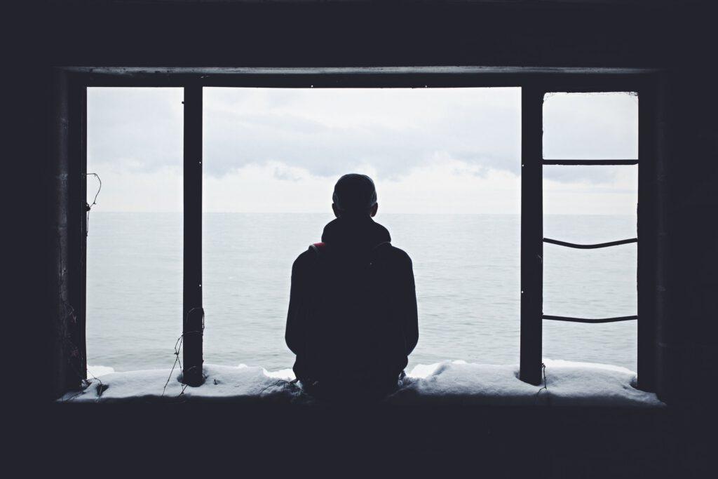 Man sits on a window sill, looking out, pensive.