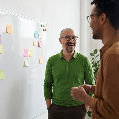 Pedro standing by a whiteboard laughing with a coaching client